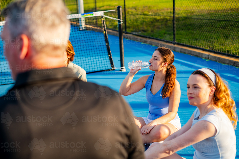Young women take a break while hydrating after tennis practice on a sunny day outdoors - Australian Stock Image