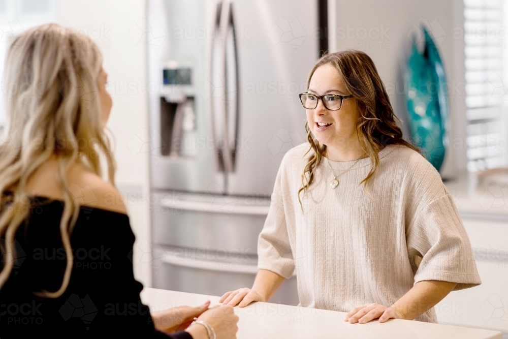 young women talking in kitchen, one sister has Down Syndrome - Australian Stock Image