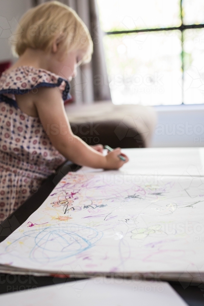 Younge blonde girl at home drawing on paper with crayons - Australian Stock Image