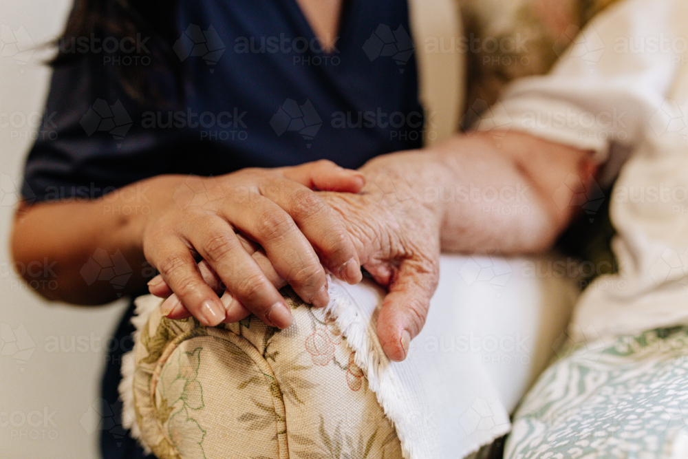 Younger hand gently resting over elderly hand on floral armrest - Australian Stock Image