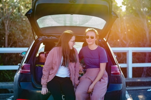 2 friends sitting on back of car - Australian Stock Image