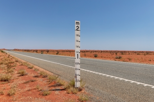 2 metre flood level marker on the edge of a long road crossing red, dry flood plain