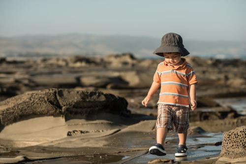 2 year old mixed race boy looks for shells on a rocky coast - Australian Stock Image