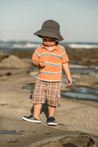 2 year old mixed race boy looks for shells on a rocky coast - Australian Stock Image