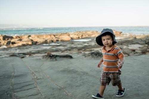 2 year old mixed race boy looks for shells on a rocky coast - Australian Stock Image