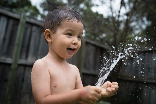 3 year old mixed race boy plays excitedly with water bombs in suburban backyard
