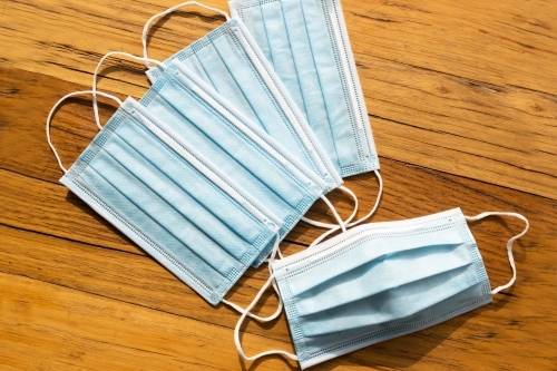 4 blue disposable surgical mask on a wooden background of PPE used during the corona virus COVID-19 - Australian Stock Image