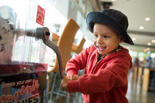 4 year old mixed race boy presses a souvenir penny at a local Sydney tourist attraction - Australian Stock Image