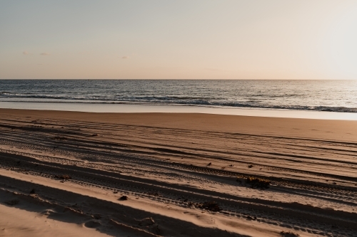 4WD tyre tracks on the beach and a calm ocean at sunset - Australian Stock Image