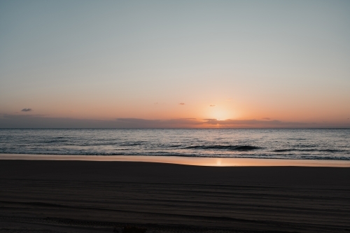 4wd tyre tracks on the beach and a calm ocean at sunset - Australian Stock Image