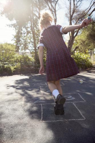 7 year old girl playing hopscotch in school uniform on asphalt - Australian Stock Image