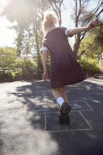 7 year old girl playing hopscotch in school uniform on asphalt