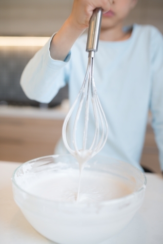 7 year old mixed race boy cooks at home with a whisk and bowl