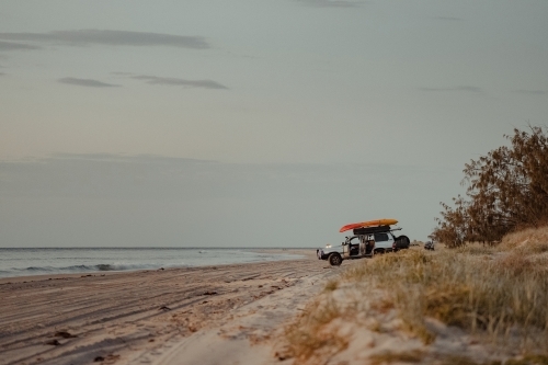 A 4WD parked on the beach for dinner at sunset near Comboyuro Point Camping Area. - Australian Stock Image