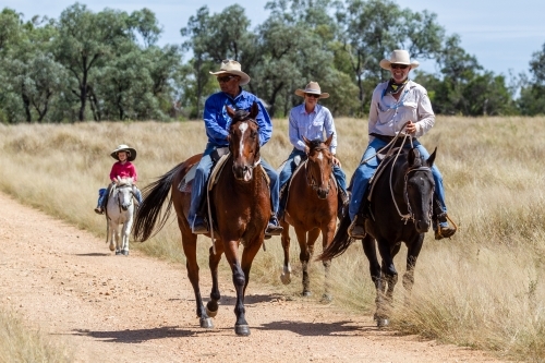 A 6 year old boy on his pony riding behind three adults on a farm.