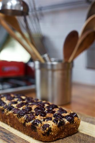 A baked cherry cake with kitchen utensils in the background