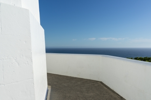 A balcony with a white balustrade, overlooking a serene sea under a clear blue sky. - Australian Stock Image