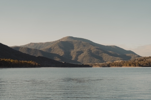 A blue lake with mountains in the background after sunrise - Australian Stock Image