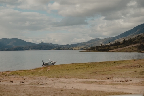 A boat at the edge of a lake with mountains in the background - Australian Stock Image