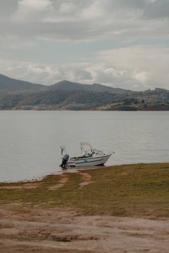 A boat at the edge of a lake with mountains in the background - Australian Stock Image