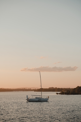 A boat sitting on the calm river at sunset near the Yamba Marina on the Clarence River. - Australian Stock Image