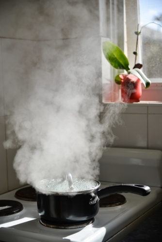 A boiling pot on a stove releases lots of steam into the morning sun - Australian Stock Image