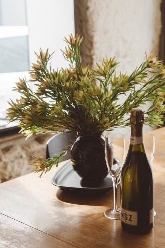 A bottle of Tasmanian sparkling wine, champagne glass and bouquet of native flowers on a table - Australian Stock Image