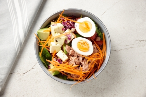 A bowl of tuna salad topped with boiled egg and cubed cheese - Australian Stock Image