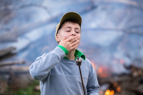 A boy eats roasted marshmallows near bonfire