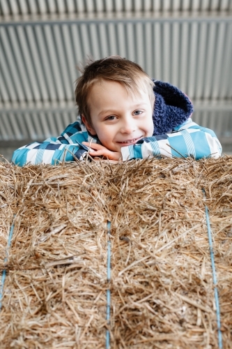 A boy lying on top of hay bales in an Australian farm shed - Australian Stock Image