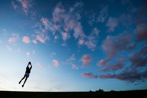 A boy plays Australian Rules Football at dusk.