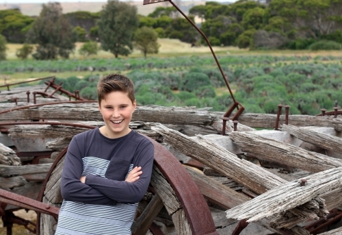 A boy smiling in front of a pile of wood and old rustic farm equipment
