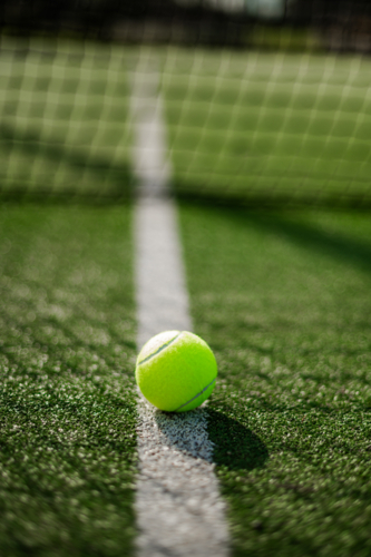 A bright green tennis ball rests near the white line on a sunlit synthetic grass court - Australian Stock Image