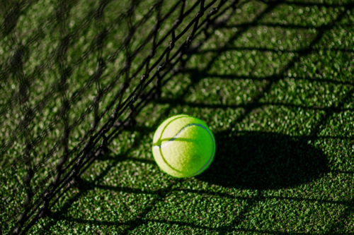 A bright green tennis ball sits on the textured synthetic grass court - Australian Stock Image