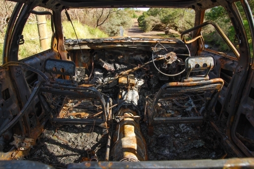 A burnt out car on a country road near a creek