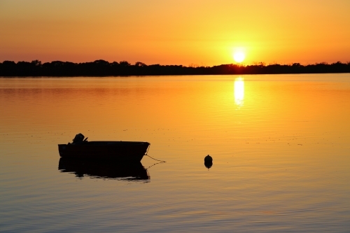 A calm golden sunrise over silhouetted dinghy on Pumicestone Passage - Australian Stock Image