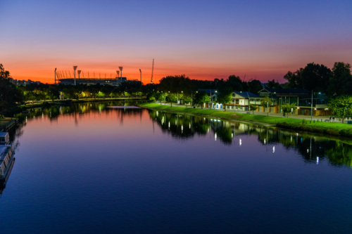 A calm river at dusk with glowing reflections and the MCG silhouetted on the horizon - Australian Stock Image