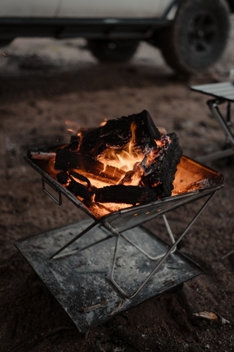 A camp fire in a fire pit in front of a four wheel drive at a camp site