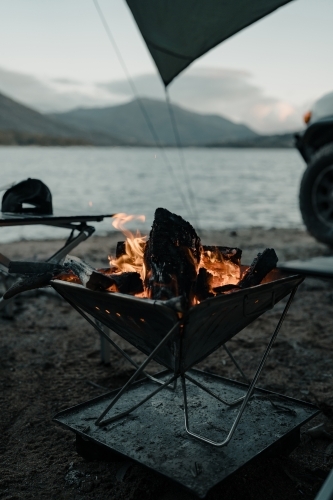 A camp fire in a fire pit in front of a lake and mountains at blue hour
