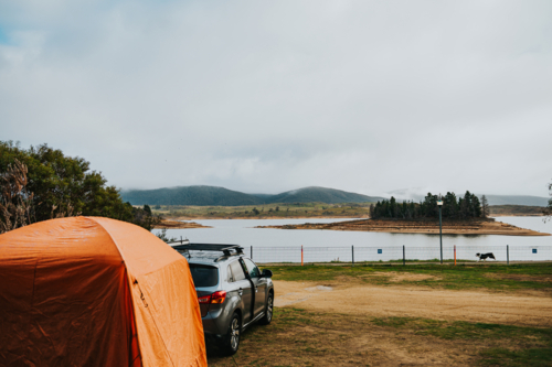 a car and a tent on a camping site in front of a lake on a winter day - Australian Stock Image