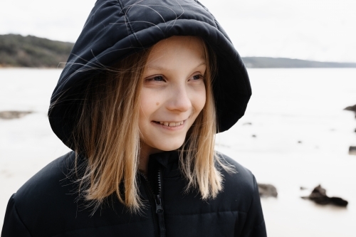 A Caucasian blonde girl wearing a warm jacket walking on a beach in winter - Australian Stock Image