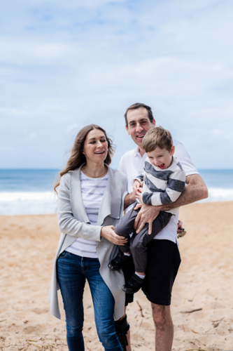 A cheerful family stands on a sandy beach, capturing a joyful moment together - Australian Stock Image