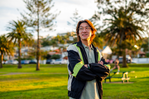 A cheerful young man stands confidently in a park surrounded by greenery and palm trees - Australian Stock Image