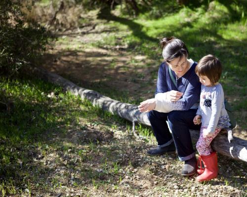 A child and her mother sitting on a branch in a dry river bed in the Australian bush - Australian Stock Image