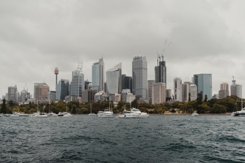 A cityscape of the Sydney on cloudy day with boats on the harbour.