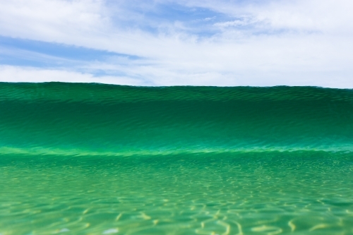 A close up of a beautiful emerald wave cresting at an Australian beach on a bright summer day