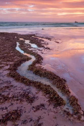 A colorful coastal sunset reflected in the water of an S shaped rock pool - Australian Stock Image