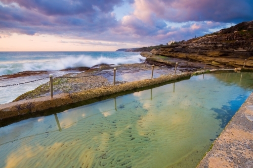 A colourful sunrise reflected in the still waters of a tidal bathing pool