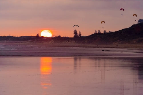 A colourful sunset reflecting on a wet beach with parasailers in the sky - Australian Stock Image