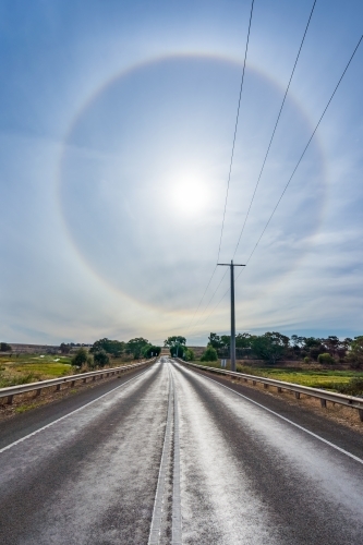 A complete Solar Halo low in the sky over a country road disappearing in the distance